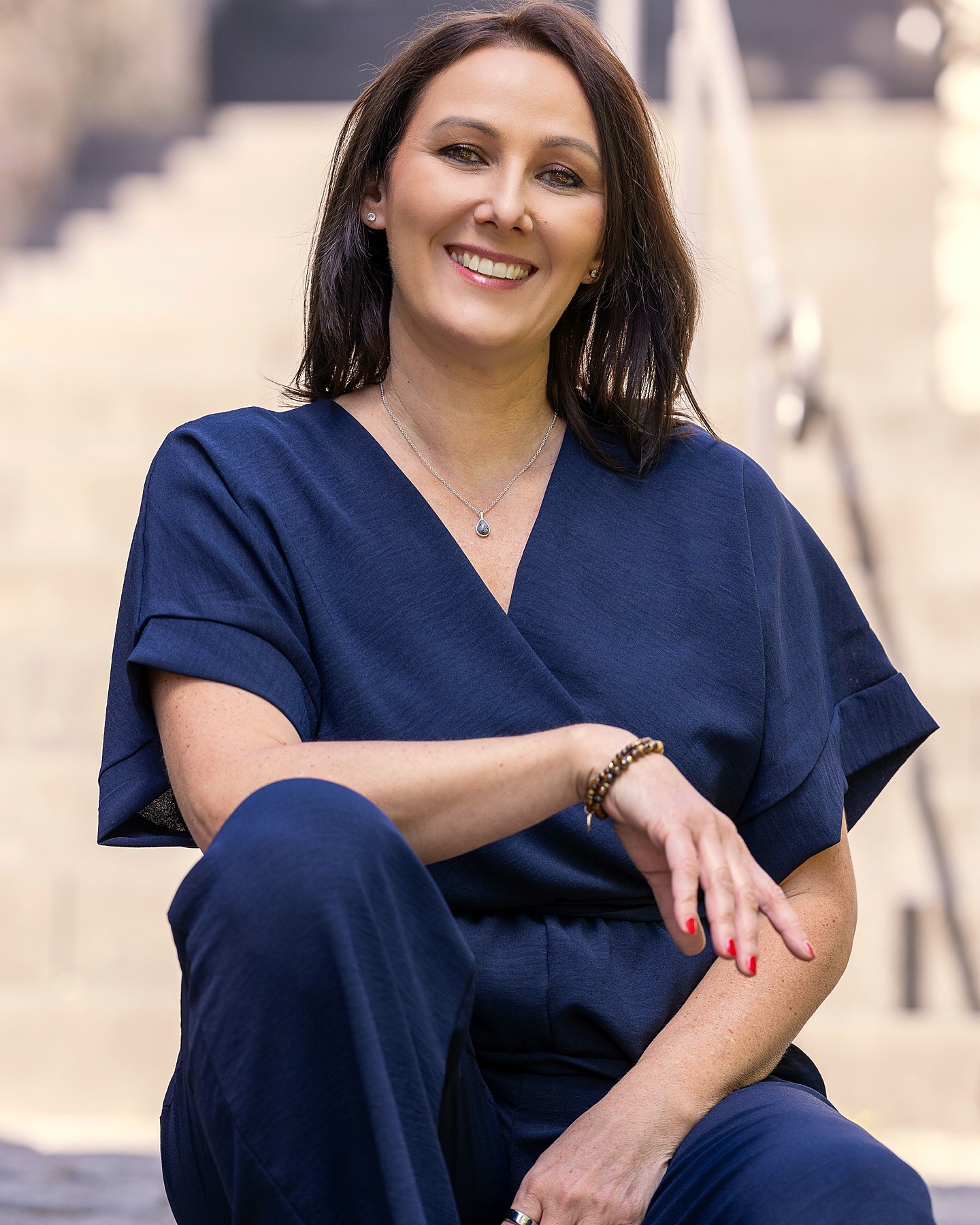 Manuela Hartmann sitzt lächelnd auf einer Steintreppe, in einem nachtblauen Overall